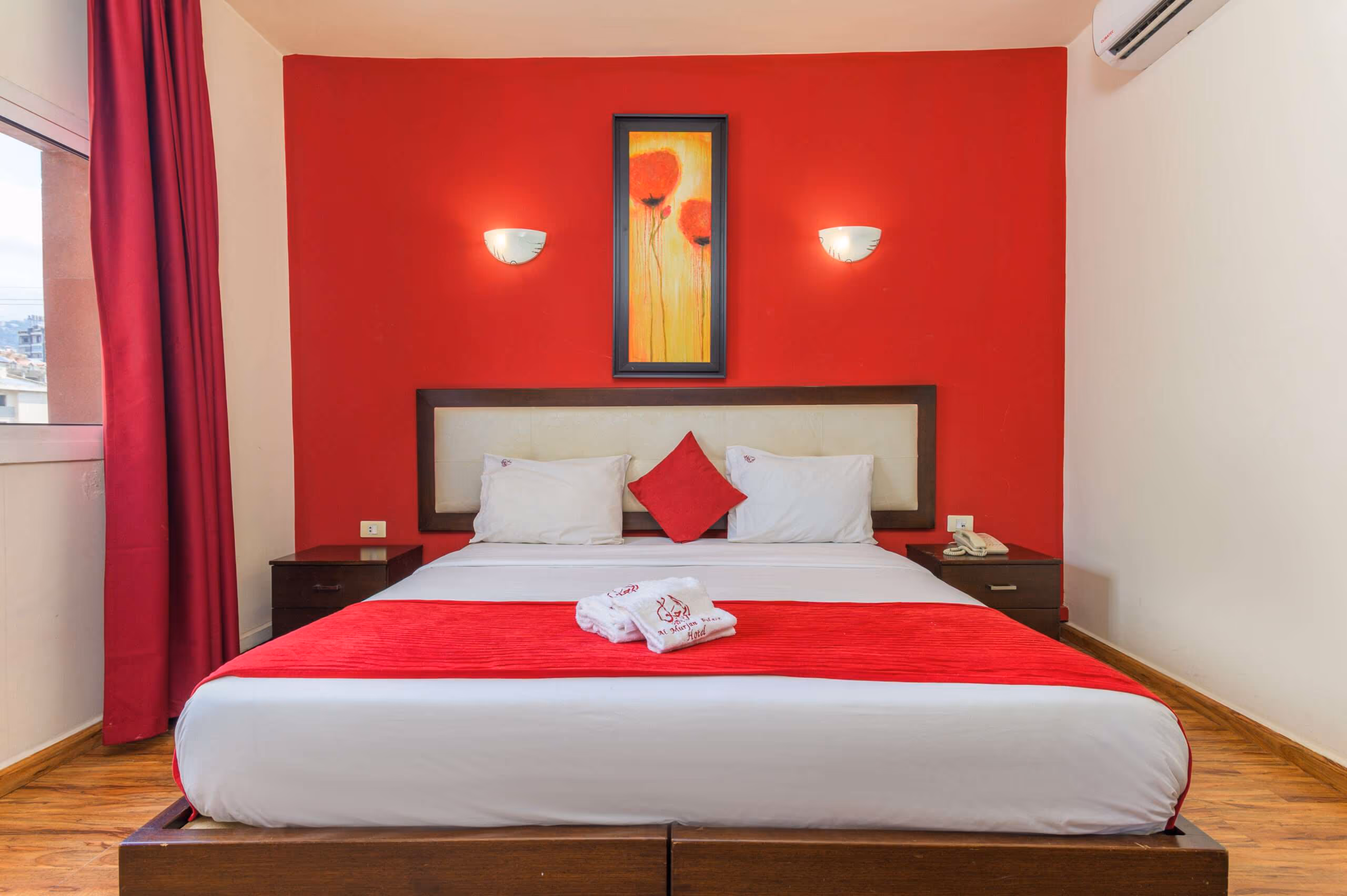 A room with a double bed against a red wall, towels folded on the bed