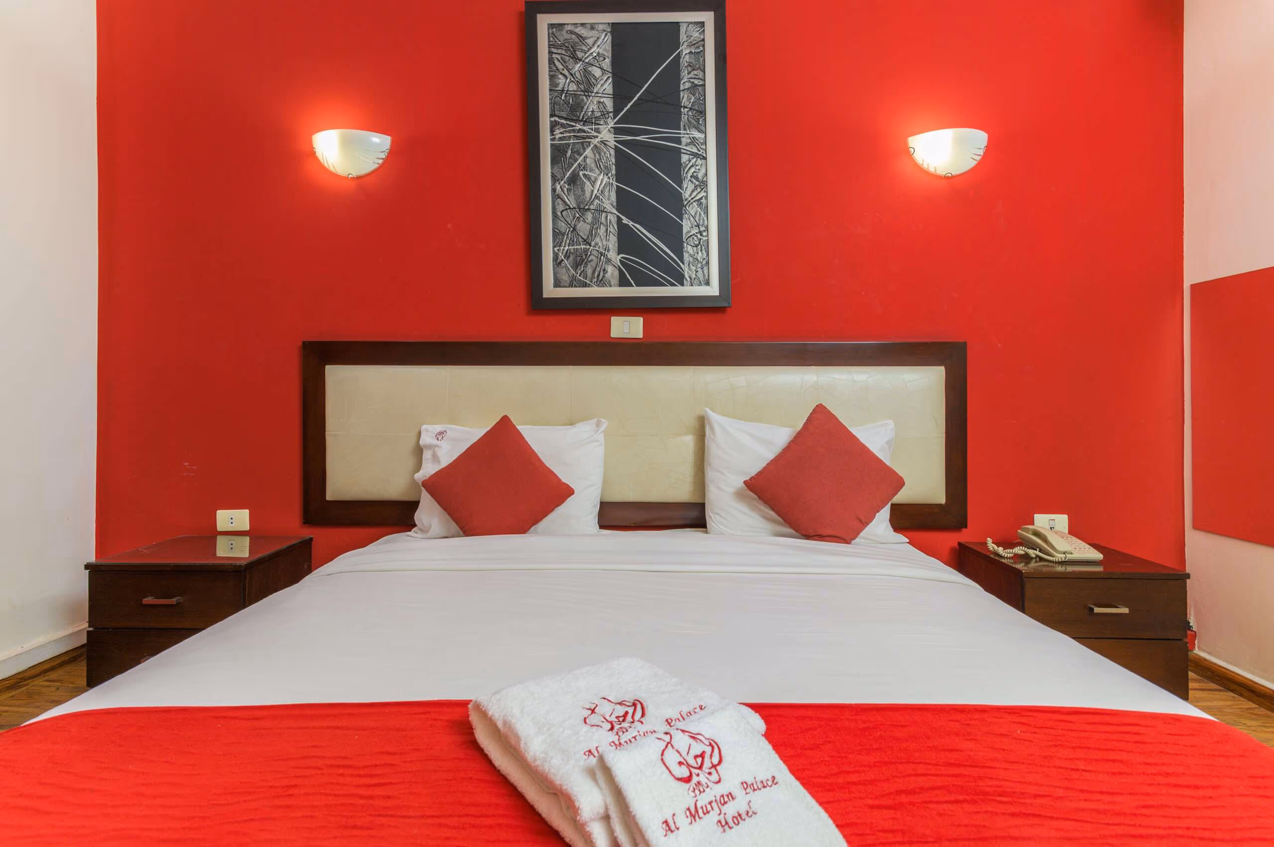 A double bed against a red wall with wall lights either side